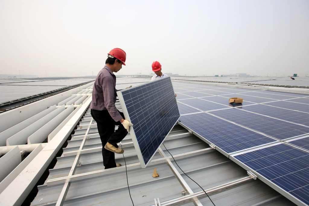 Installers carrying a solar panel into place on a metal roof